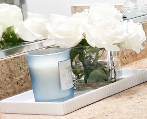 Decor for Primary Bathroom Vanity with a white vanity tray. White Roses in a square glass vase with a candle in a blue container.